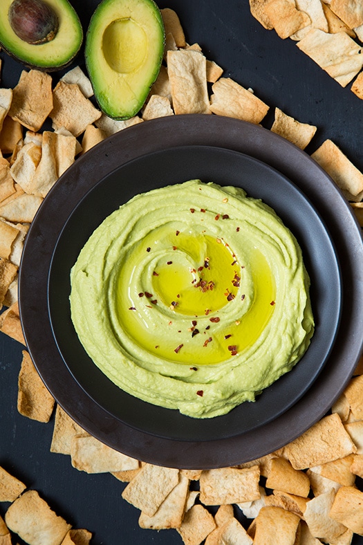 Avocado hummus in a bowl with sliced avocado at the side