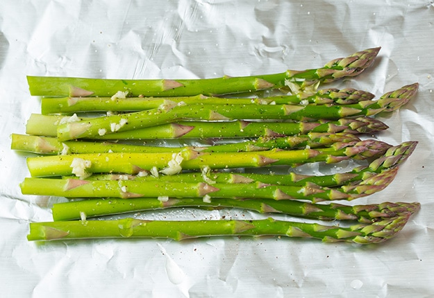 Laying asparagus on sheet of foil before topping with salmon.