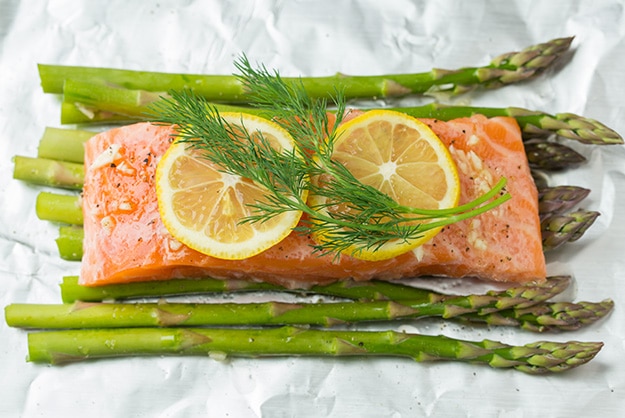 Adding lemon slices and fresh dill over salmon fillet.