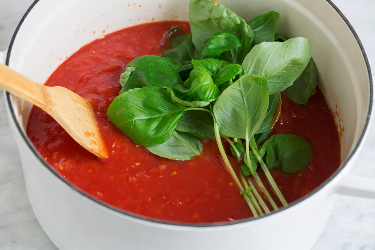 Adding crushed tomatoes and fresh basil to pot.