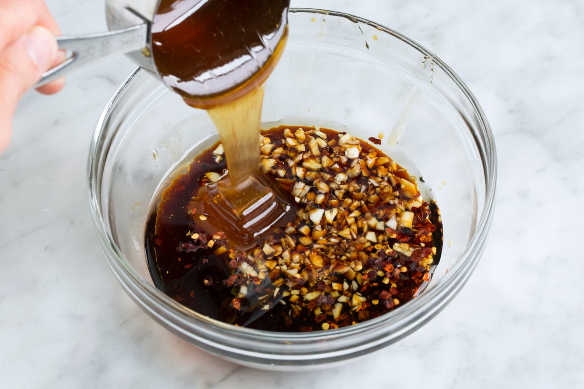 Showing how to make shrimp marinade. Mixing soy sauce, garlic, olive oil and honey in a glass mixing bowl.
