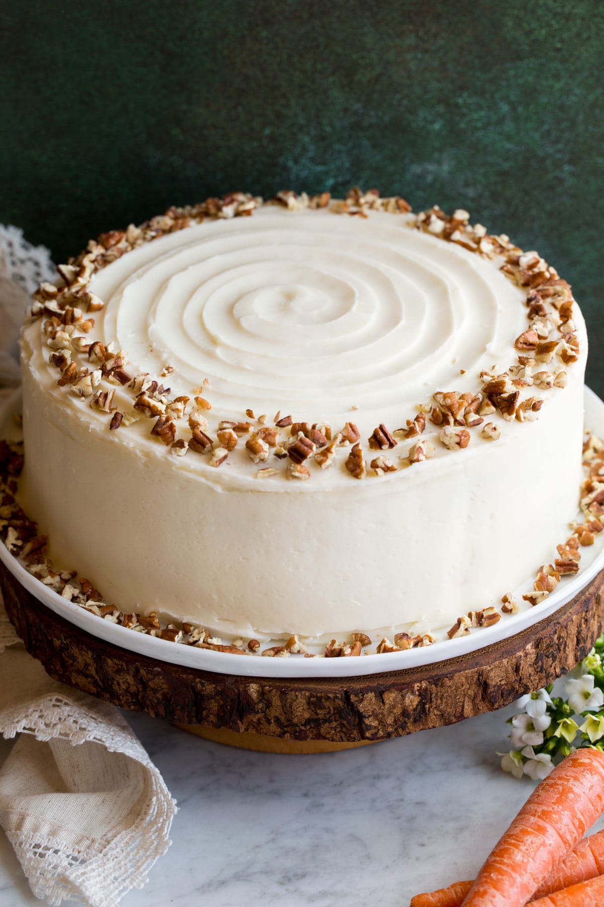 Whole carrot cake sitting on a wooden cake stand.