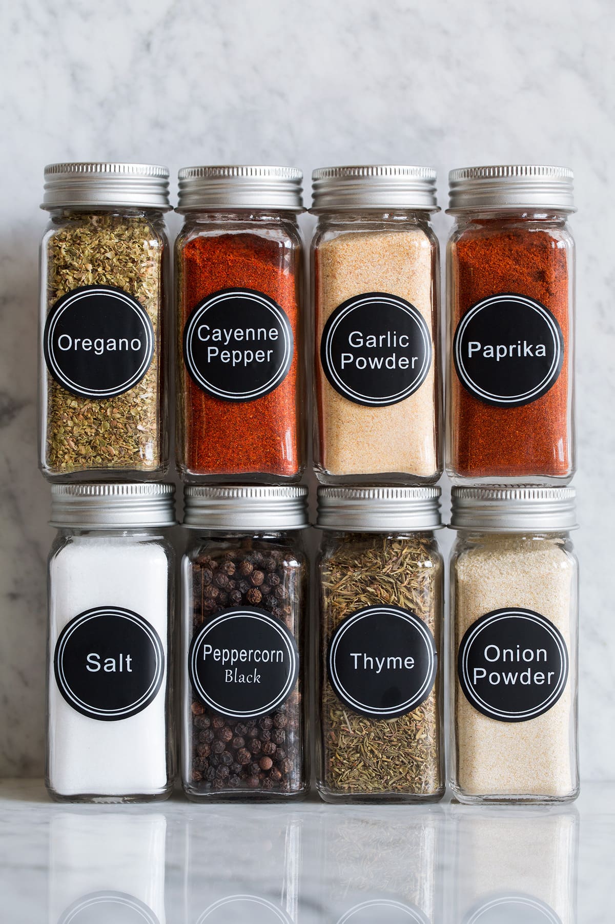 Photo: Eight glass jars of spices that are used to make cajun seasoning shown on a marble surface.
