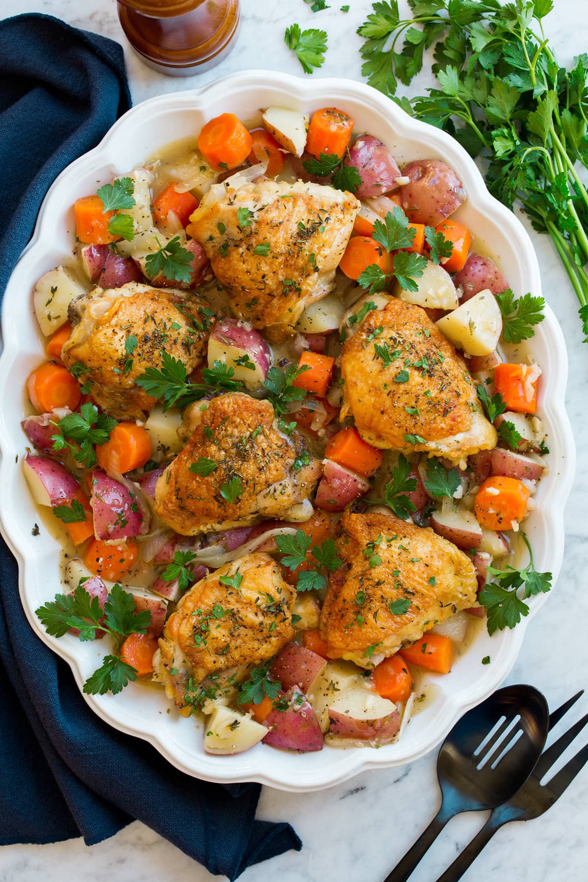 Braised chicken and vegetables on a white oval platter on a marble surface..