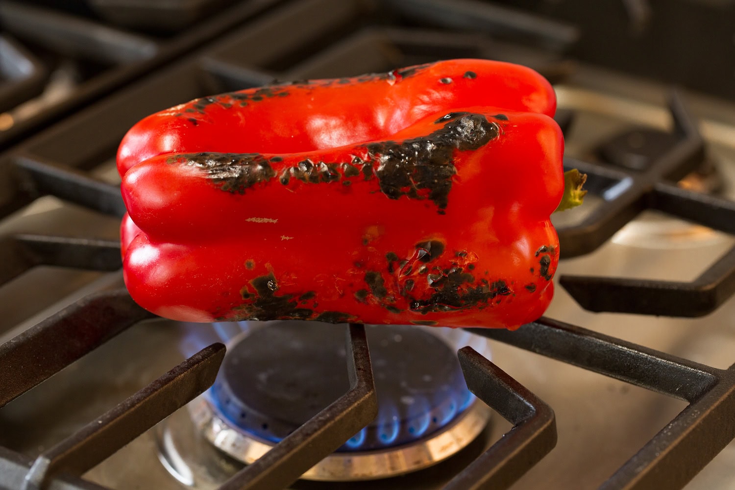 Bell pepper being roasted over flame of gas stove.