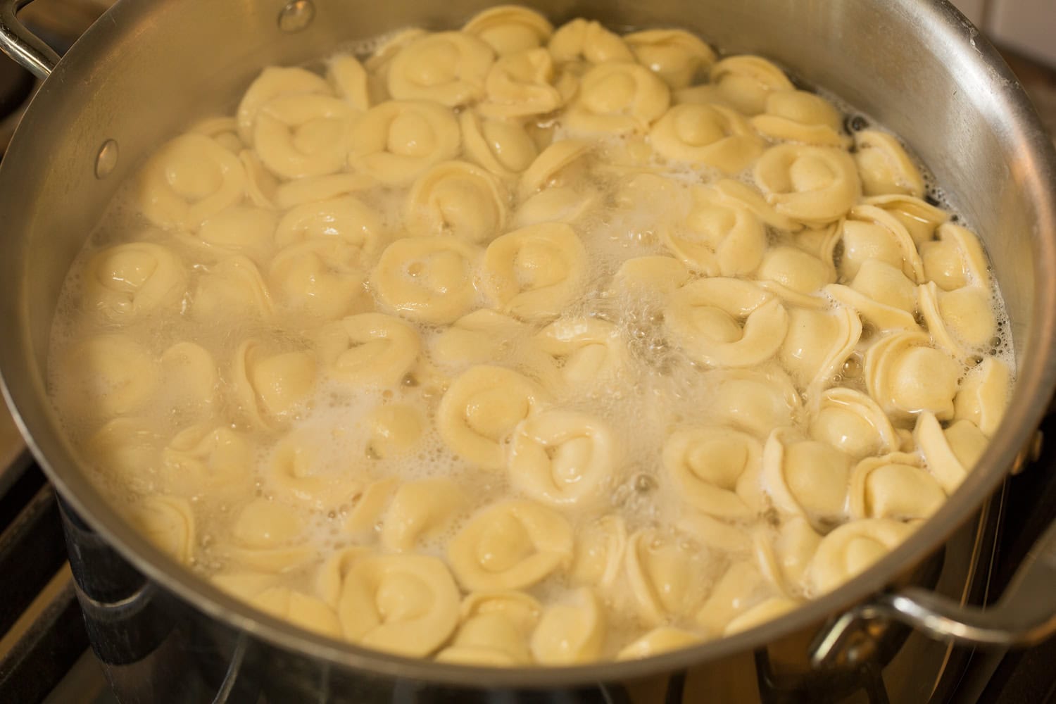 Tortellini being cooked in boiling water in a stainless pot.