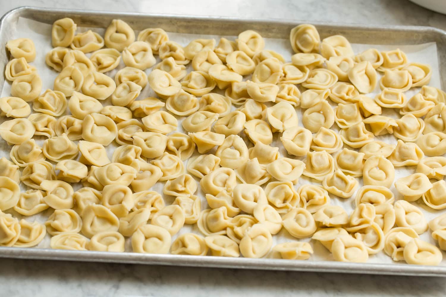 Tortellini pasta salad cooling on a baking sheet.